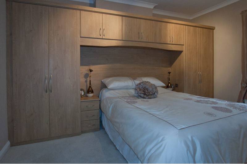 beige bedroom with custom-built overbed cupboards and wardrobes in pine colour